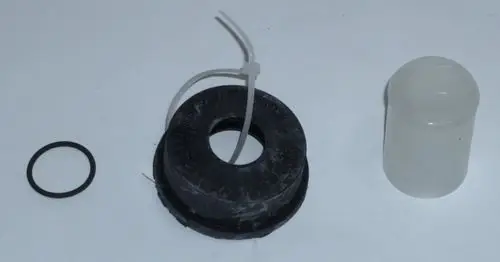 Daikin Schlauchanschluss und Zubehörteile, darunter ein schwarzes Gummi-Element mit mittigem Loch, eine transparente Abdeckung und ein schwarzer O-Ring.